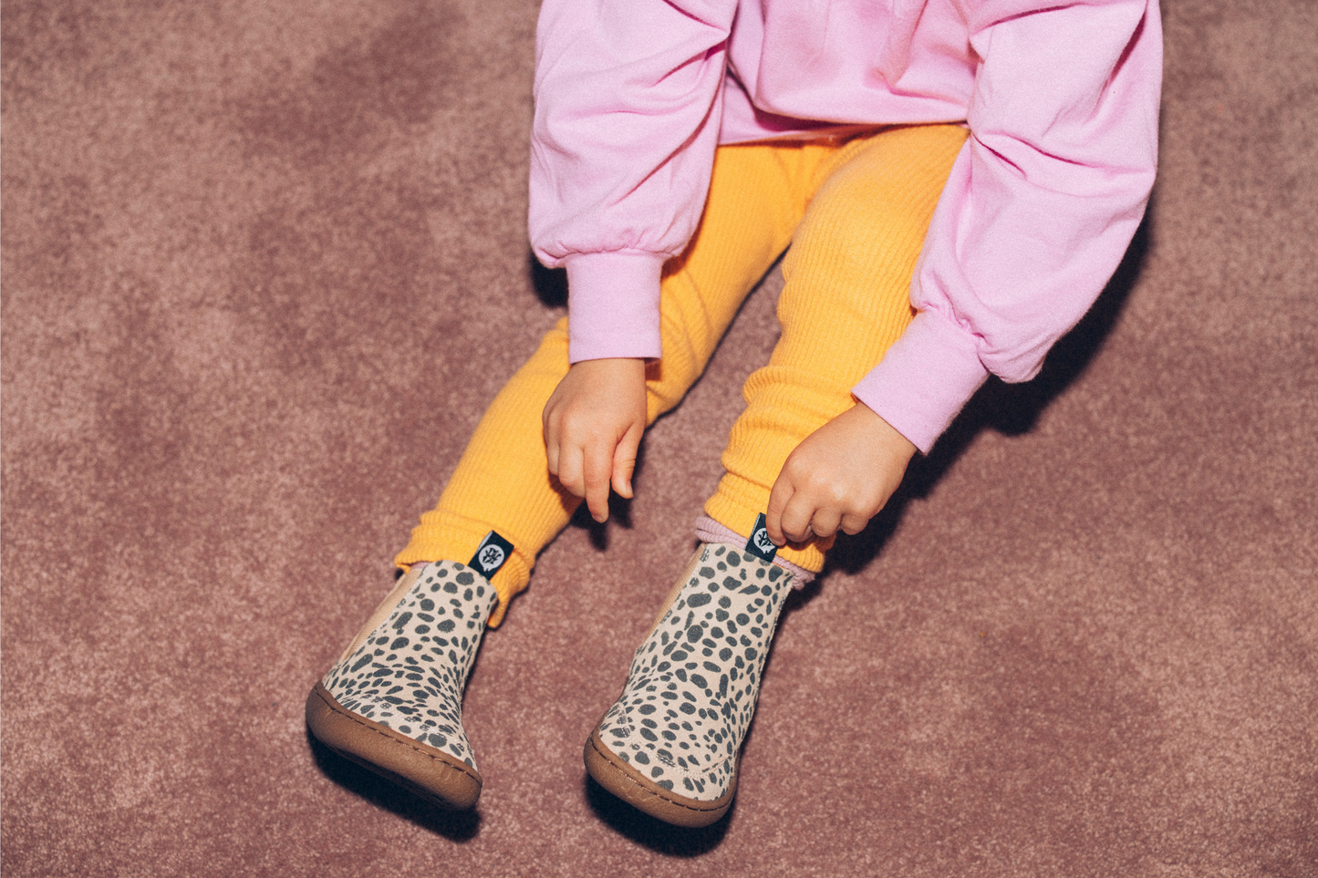 CHILD SITTING AND TOUCHING TAG ON CHEETAH BOOTS