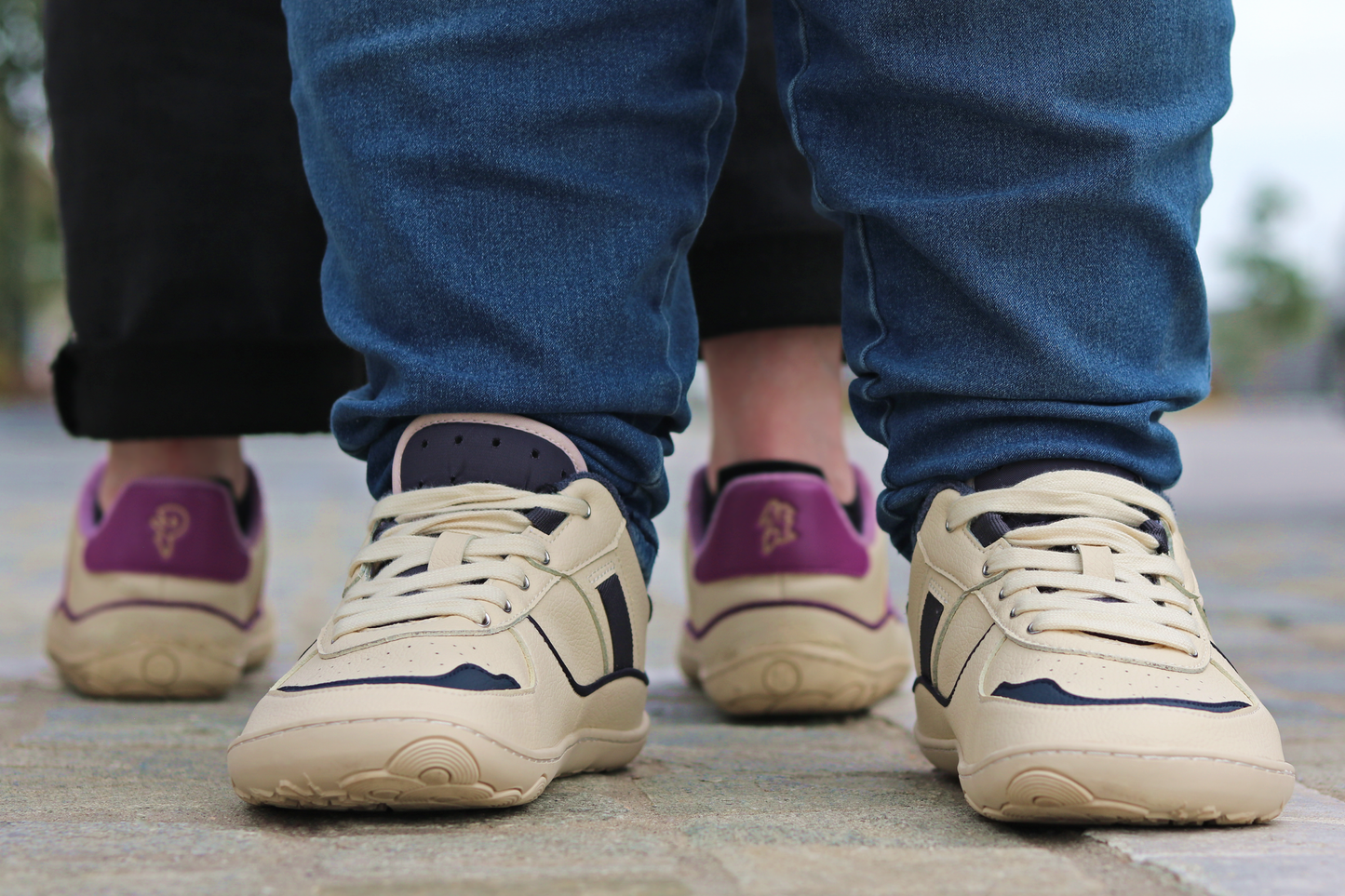 FRONT VIEW OF INKY ON A WIDER FOOT, WITH THE BACK OF SOME PLUM SNEAKERS BEHIND