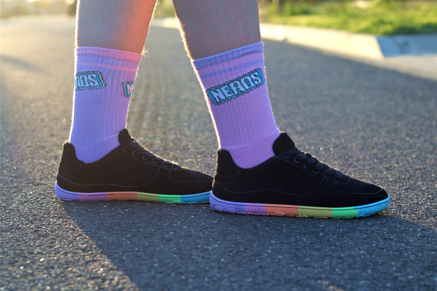 Person wearing black sneakers with rainbow soles and purple socks with 'NERDS' branding on a road.