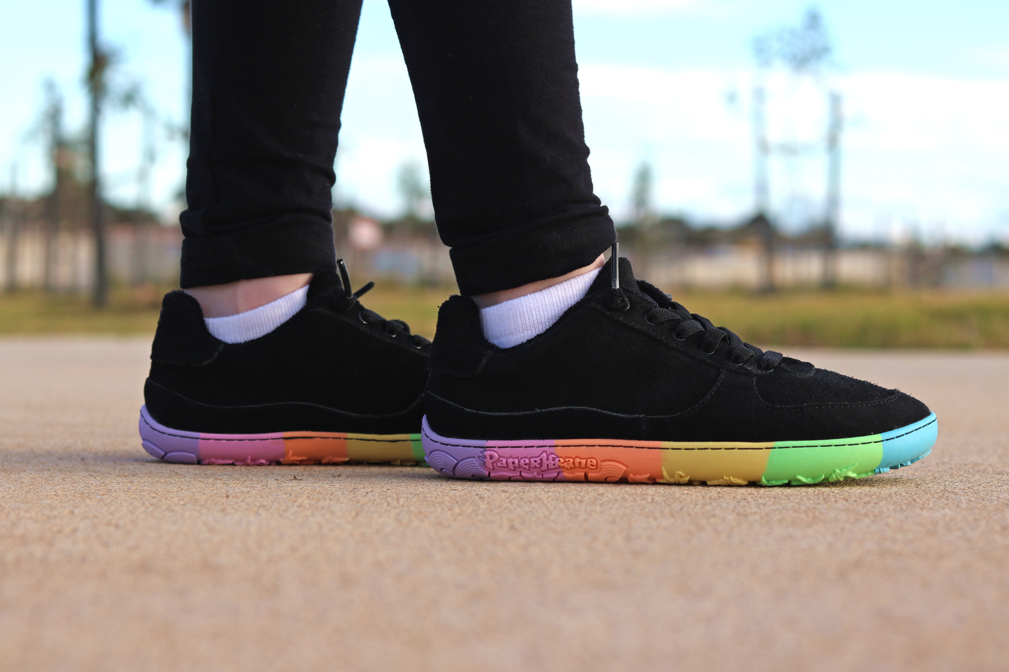 Black sneakers with colourful soles worn outdoors on a blurred background