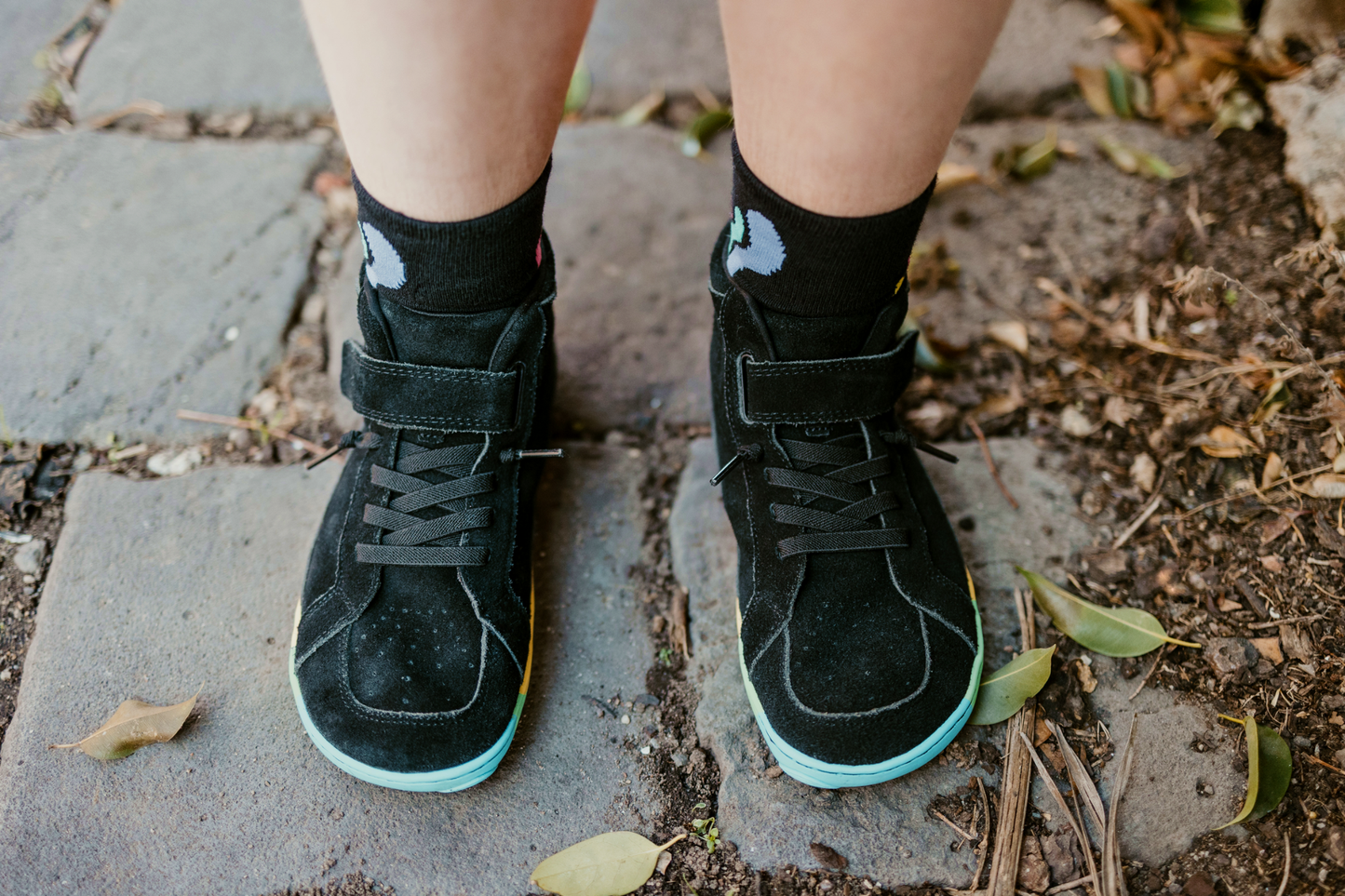 Black mid-top sneakers with rainbow soles on a concrete surface.