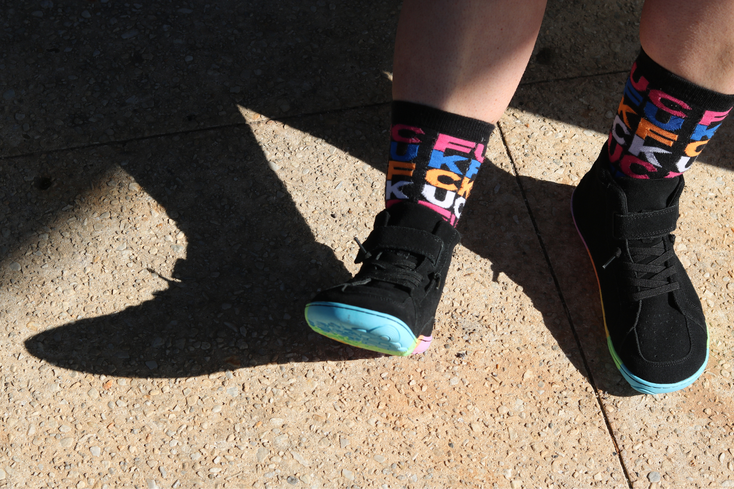 Person wearing black sneakers with colourful text socks on a concrete surface