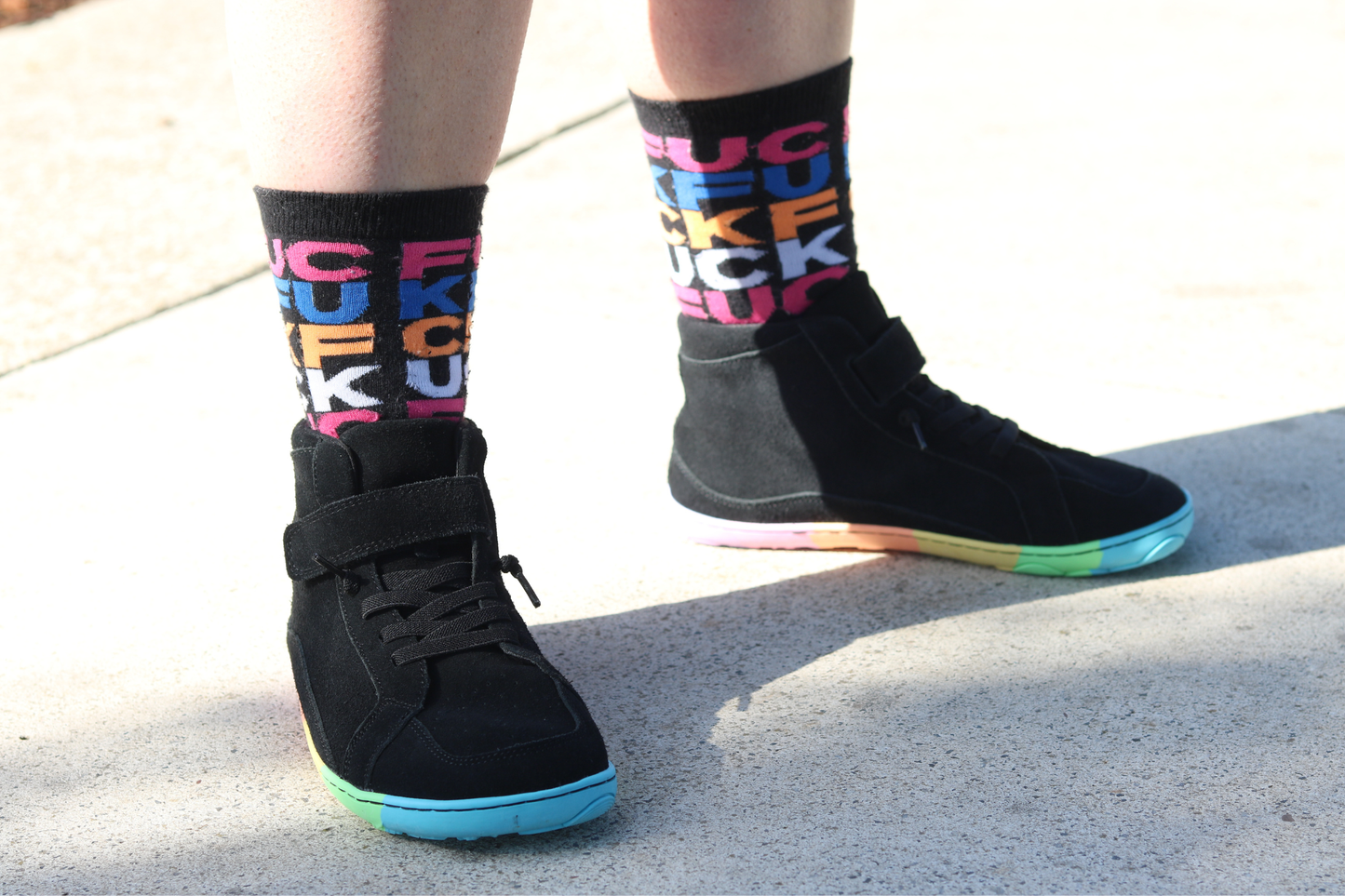 Black mid-top sneakers with colourful text socks on a light background