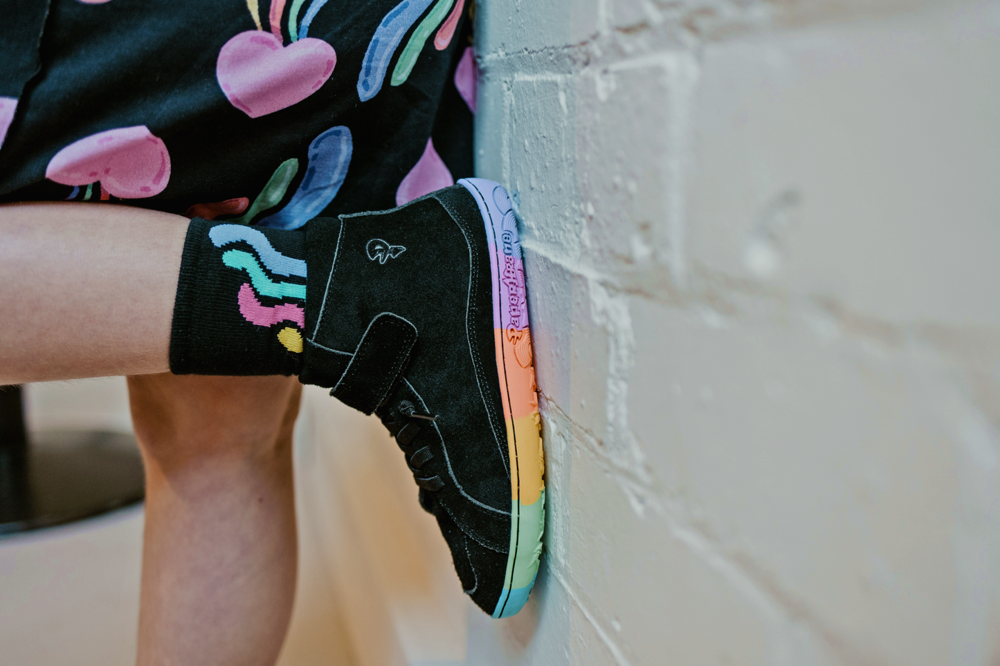 Person wearing a colourful sock with a rainbow sole against a tiled wall.