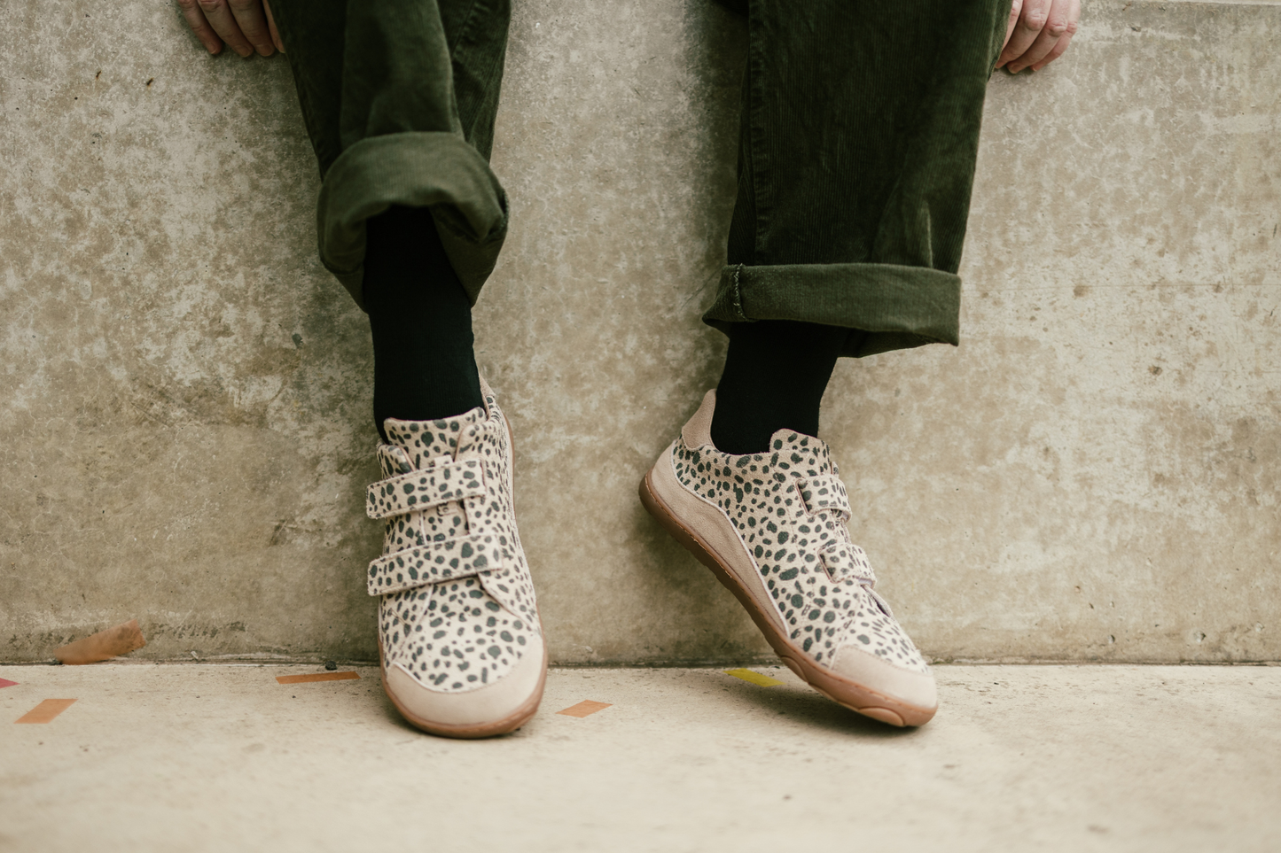 Person wearing cheetah print sneakers with green pants against a concrete wall.