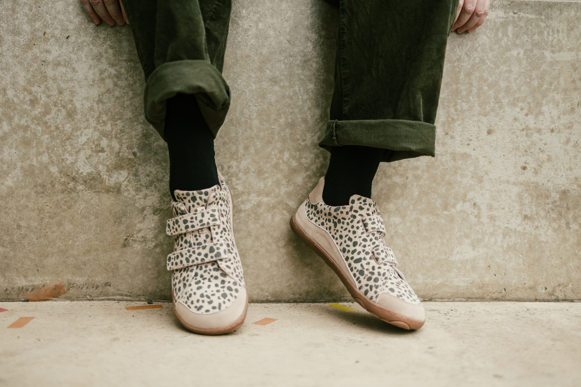 Person wearing cheetah print sneakers with green pants against a concrete wall.
