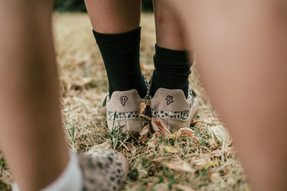 Close-up of feet wearing sneakers with cheetah patterns on grassy ground.
