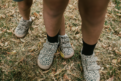 Children's feet wearing cheetah print shoes on grassy ground