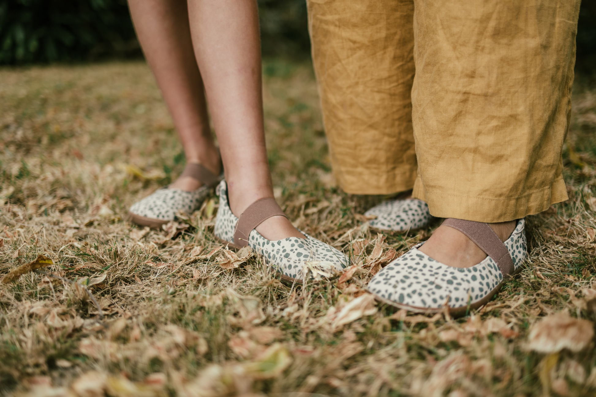 Two pairs of feet (child and adult) in matching wearing cheetah patterned shoes on grassy ground.