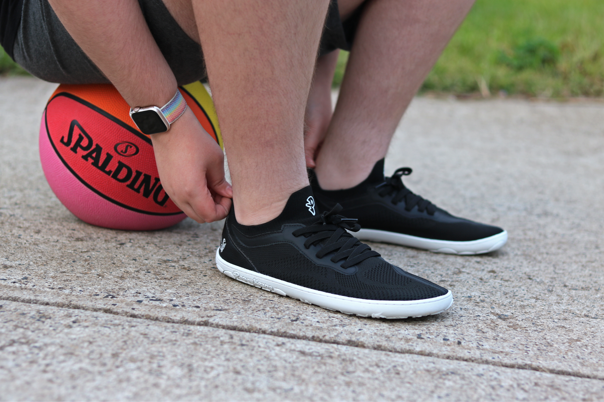PERSON SITTING ON A RAINBOW BASKETBALL PULLING ON THEIR AKTIVE LOW SNEAKER