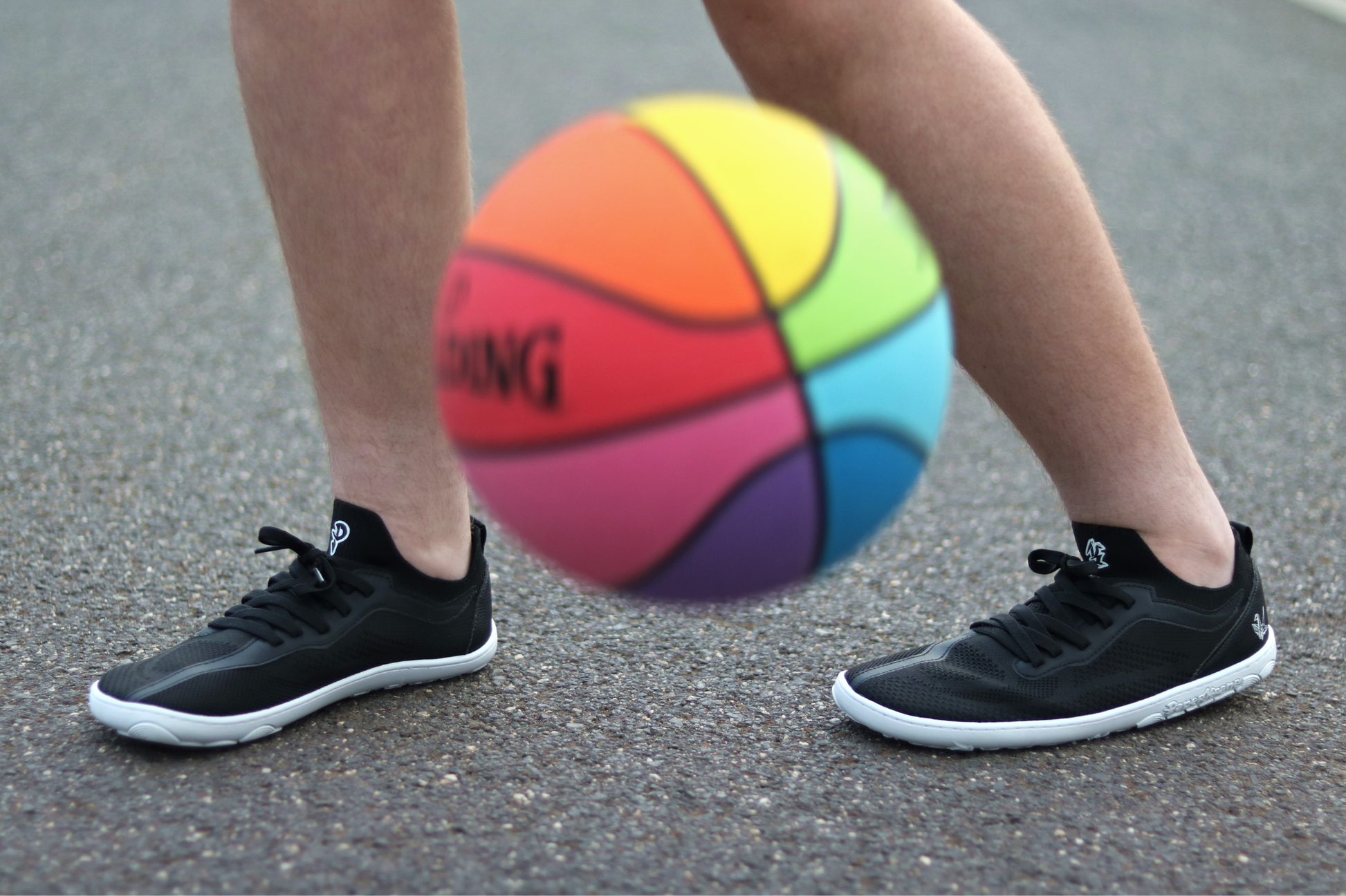 Person wearing black PaperKrane AKTIVE sneakers with a colourful basketball on a gray surface