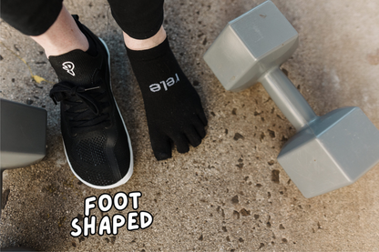 Person wearing black toe socks with PaperKrane foot-shaped shoes on a concrete surface with dumbbells.