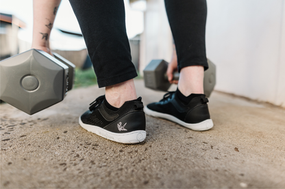 Person lifting weights wearing black barefoot sneakers on a concrete surface.