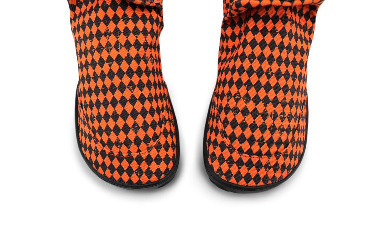 A close-up view from above of a pair of slip-on shoes featuring a bold orange and black harlequin diamond pattern, shown against a plain white background.