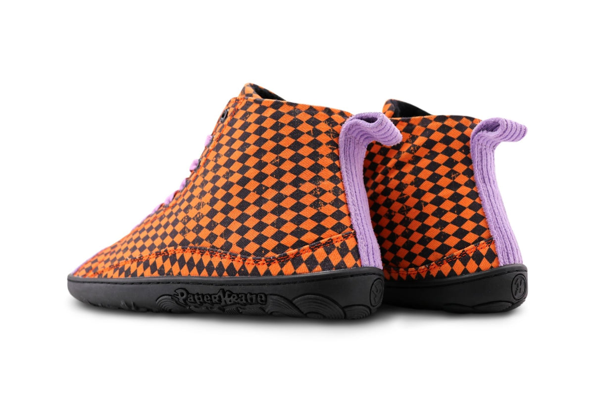 A pair of PaperKrane barefoot tall boots with orange and black argyle printed cotton uppers, with purple corduroy toe and heel, on a black rubber sole can be seen from the back on a white background. 