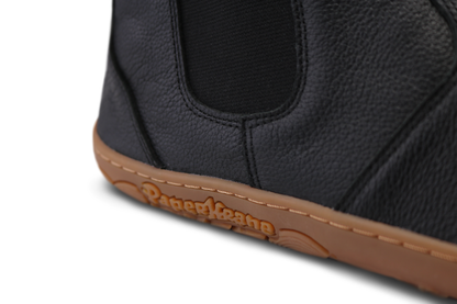 Close up view of the side of the gum sole with "PaperKrane" on the side. The chelsea boot is a textured black leather and on a white background. 