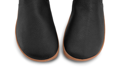 Above view of the toe-box of a pair of foot-shaped barefoot black leather chelsea boots from PaperKrane. The leather is textured, and the sole is a natural gum colour. 