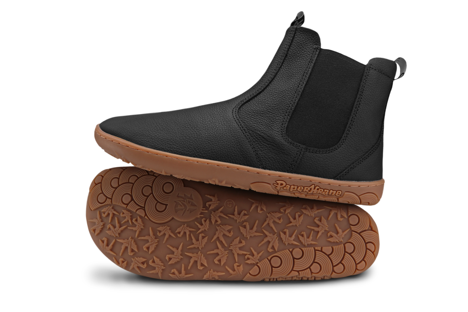 Black leather barefoot PaperKrane chelesa boots with gum soles on a white background. The view is of the side of one boot which sits on top of the other boot where you can see the foot-shaped sole and PaperKrane sole details. 