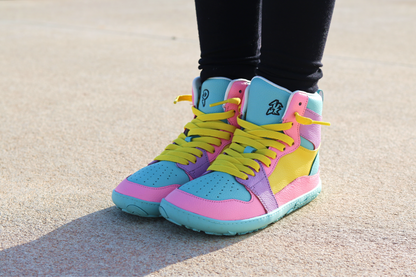 Colourful high-top sneakers with pink, blue, and yellow accents worn on a concrete surface.