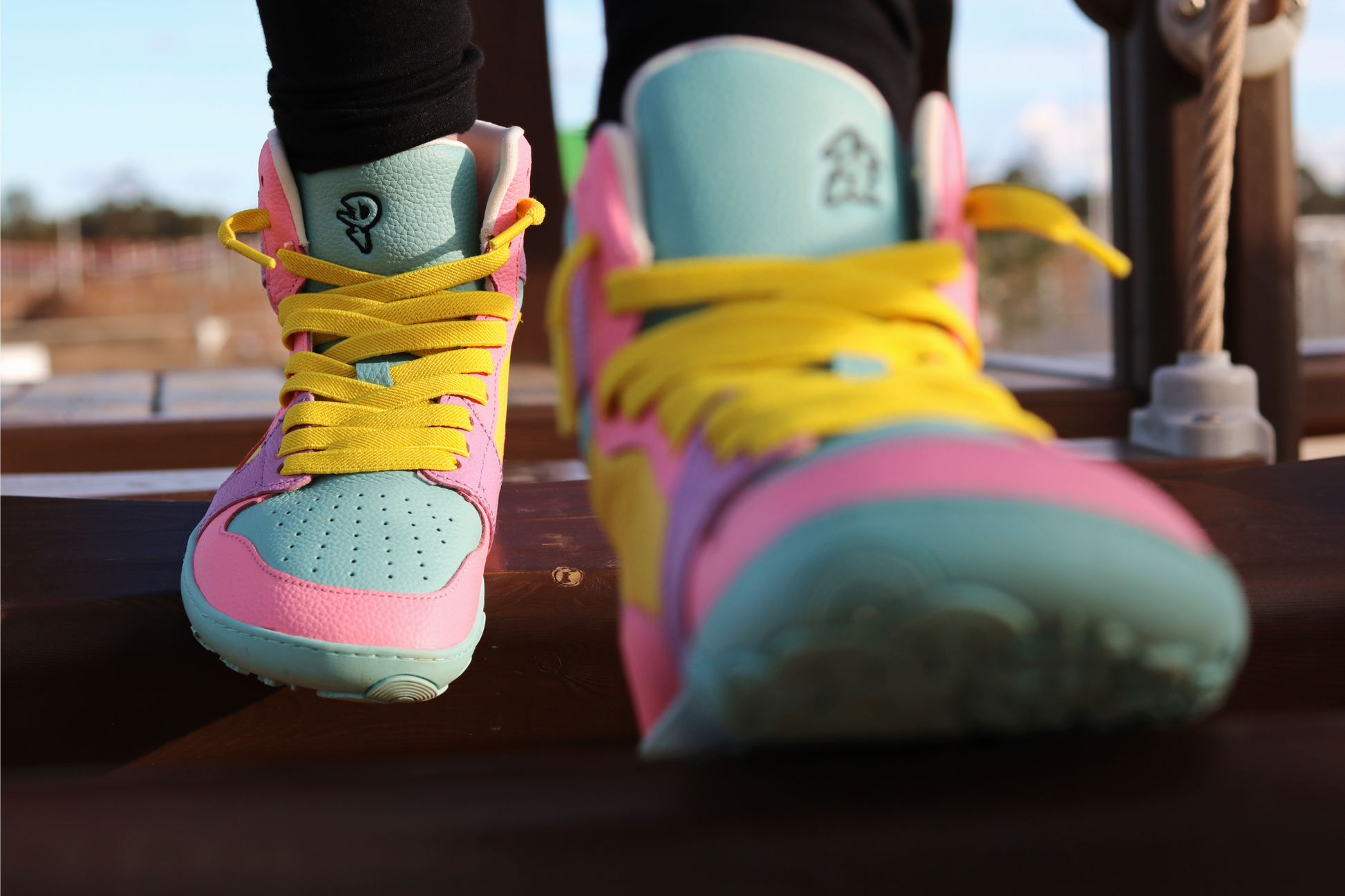 Colourful high top sneakers with pink, yellow, and light blue design on a blurred outdoor background