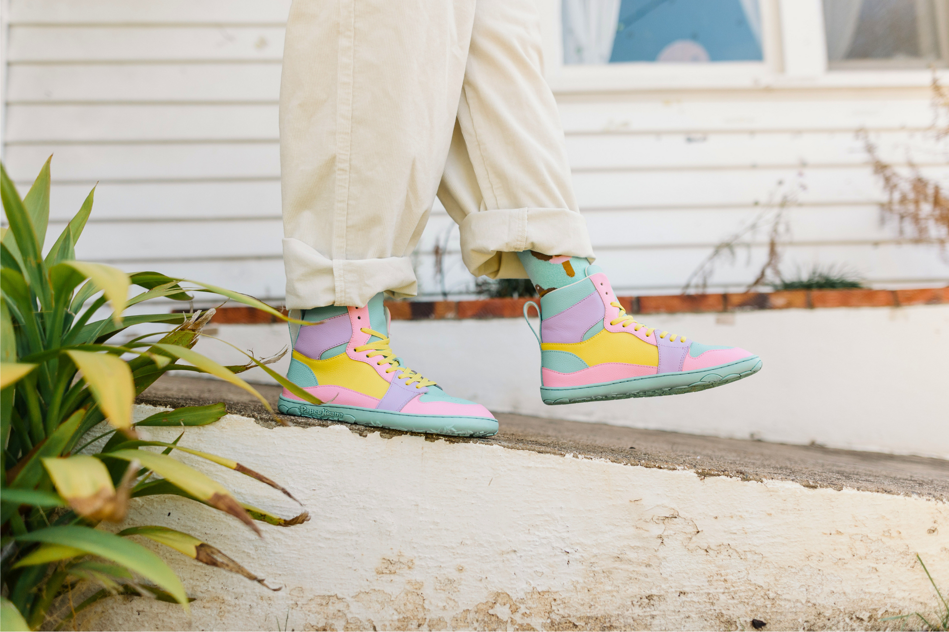 Colourful high-top sneakers worn with light-colored pants on a concrete surface.