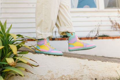 Colourful high-top sneakers worn with light-colored pants on a concrete surface.