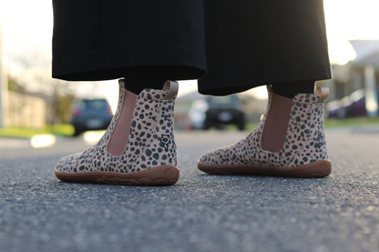 A person wearing cheetah-print Chelsea-style boots with tan elastic side panels, standing on asphalt outdoors.