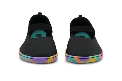 A pair of black slip-on foot-shaped mary janes from PaperKrane with colourful rainbow-patterned soles and teal insoles, shown from the front of the toe box on a white background.