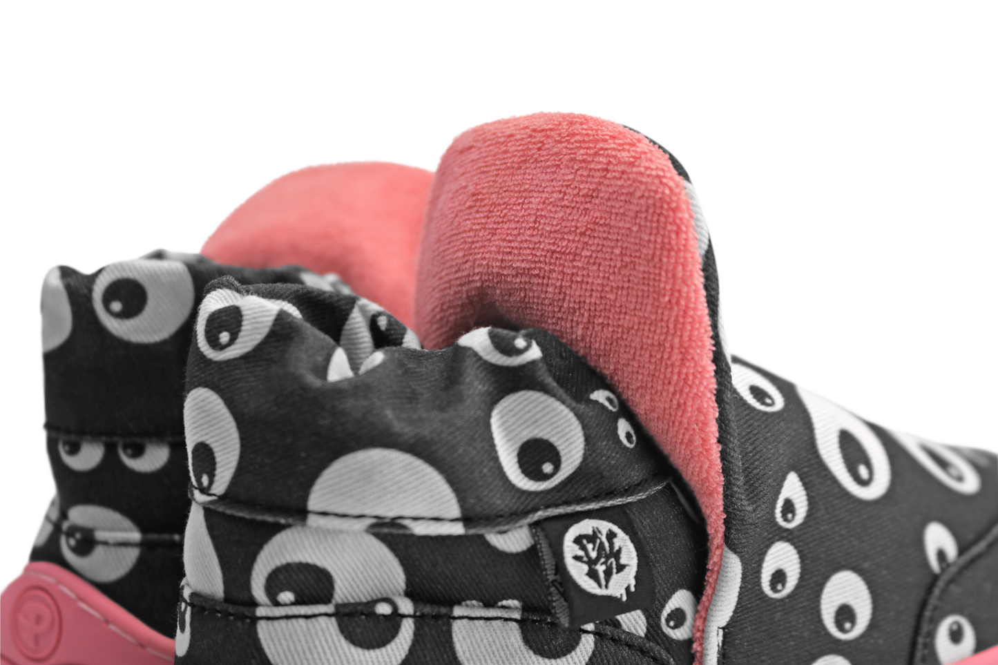 Up close of the terry cotton lining behind the pop up tongue on these PaperKrane Signature slip on high tops. The black cotton has cartoon eyeballs printed on it, and you can see a little bit of the salmon coloured rubber sole. The shoes are on a white background. 