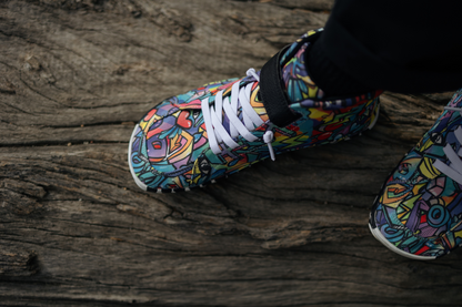 PaperKrane foot-shaped Mid Top barefoot shoes with graffiti print on cotton, black velcro strap, and zebra soles. Another view from above the shoes, this time standing on a log with one foot in front of the other. The person is wearing black socks and pants. 