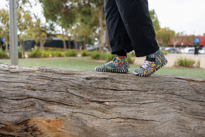 PaperKrane foot-shaped Mid Top barefoot shoes with graffiti print on cotton, black velcro strap, and zebra soles. An adult in black pants is walking on top of a log to show how balanced you are in barefoot shoes, and to show off the fun graffiti print on the shoes. 