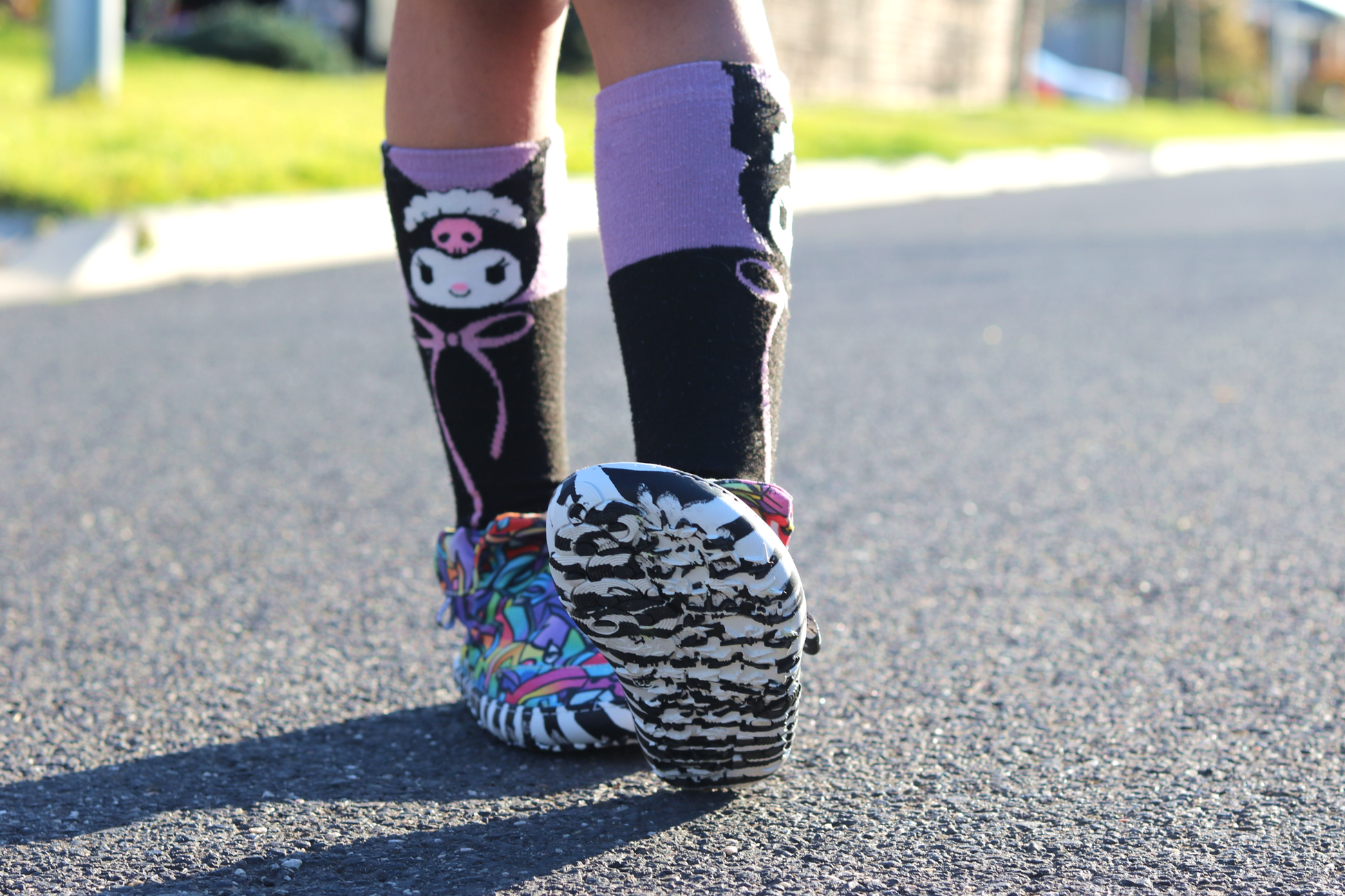 PaperKrane Graffiti signature style barefoot shoe slip ons, with hand-drawn graffiti print and zebra soles, on a child who is walking on the road, the foot-shaped nature of the toe box is clear.