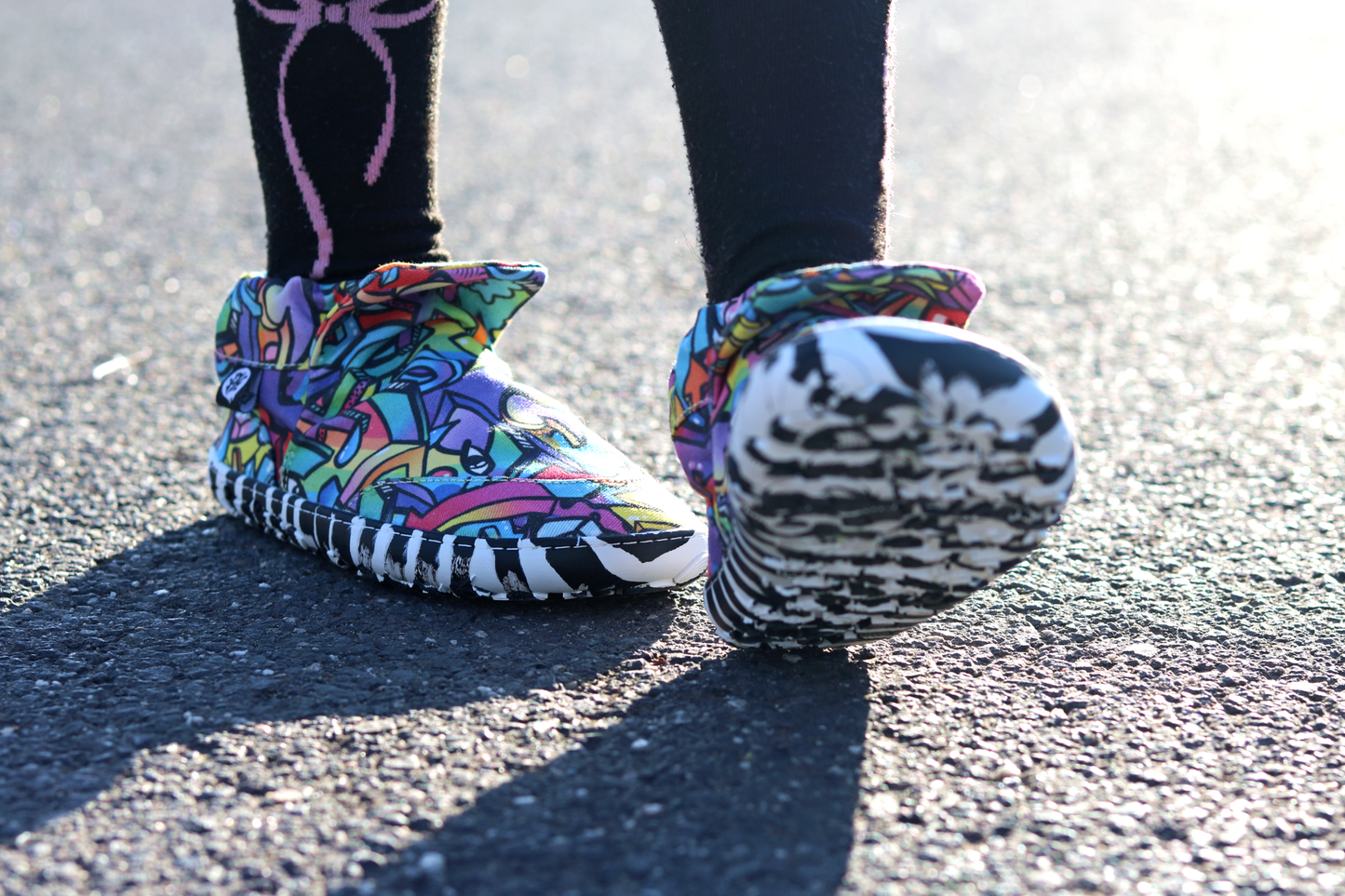 PaperKrane Graffiti signature style barefoot shoe slip ons, with hand-drawn graffiti print and zebra soles, on a child who is walking on pavement.
