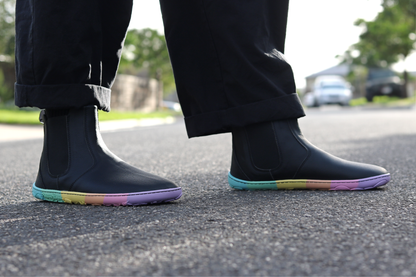 Black vegan leather chelsea boot from PaperKrane with rainbow zero drop sole standing in the street. 