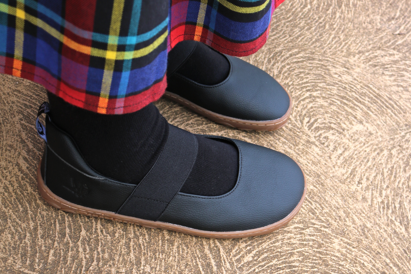 Side view of black and gum mary janes with black socks and tartan skirt. 