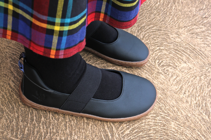 Side view of black and gum mary janes with black socks and tartan skirt. 