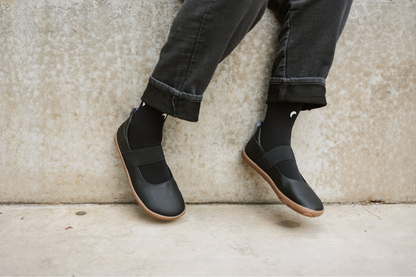Legs in black with black vegan leather mary janes on concrete background. 
