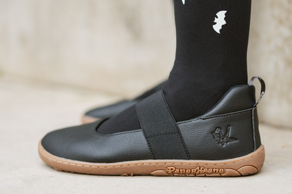 Side view of black vegan leather mjs with gum sole, and visible PaperKrane logo, on concrete.