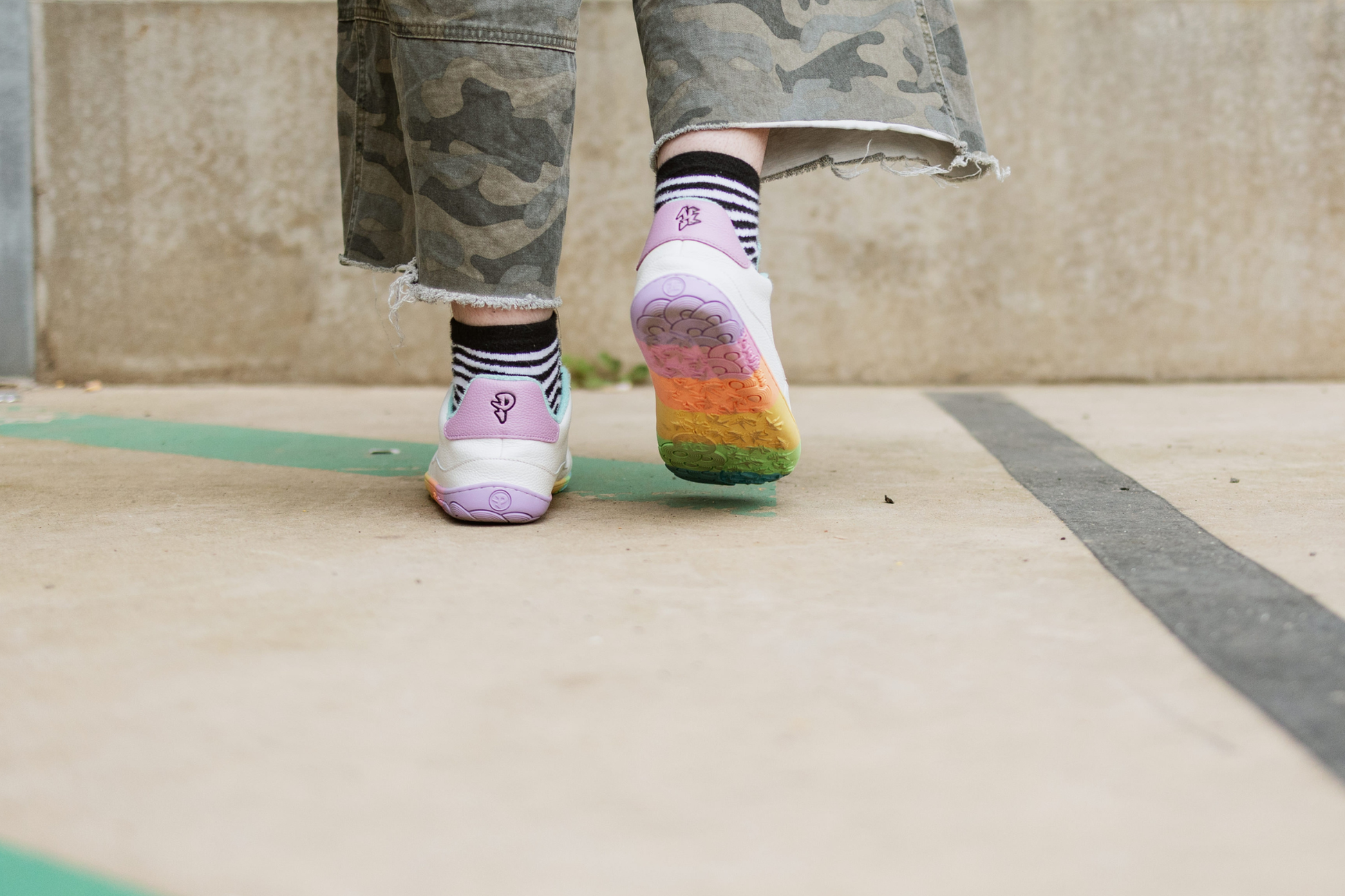 Person wearing colourful soles with a rainbow pattern on a concrete surface.