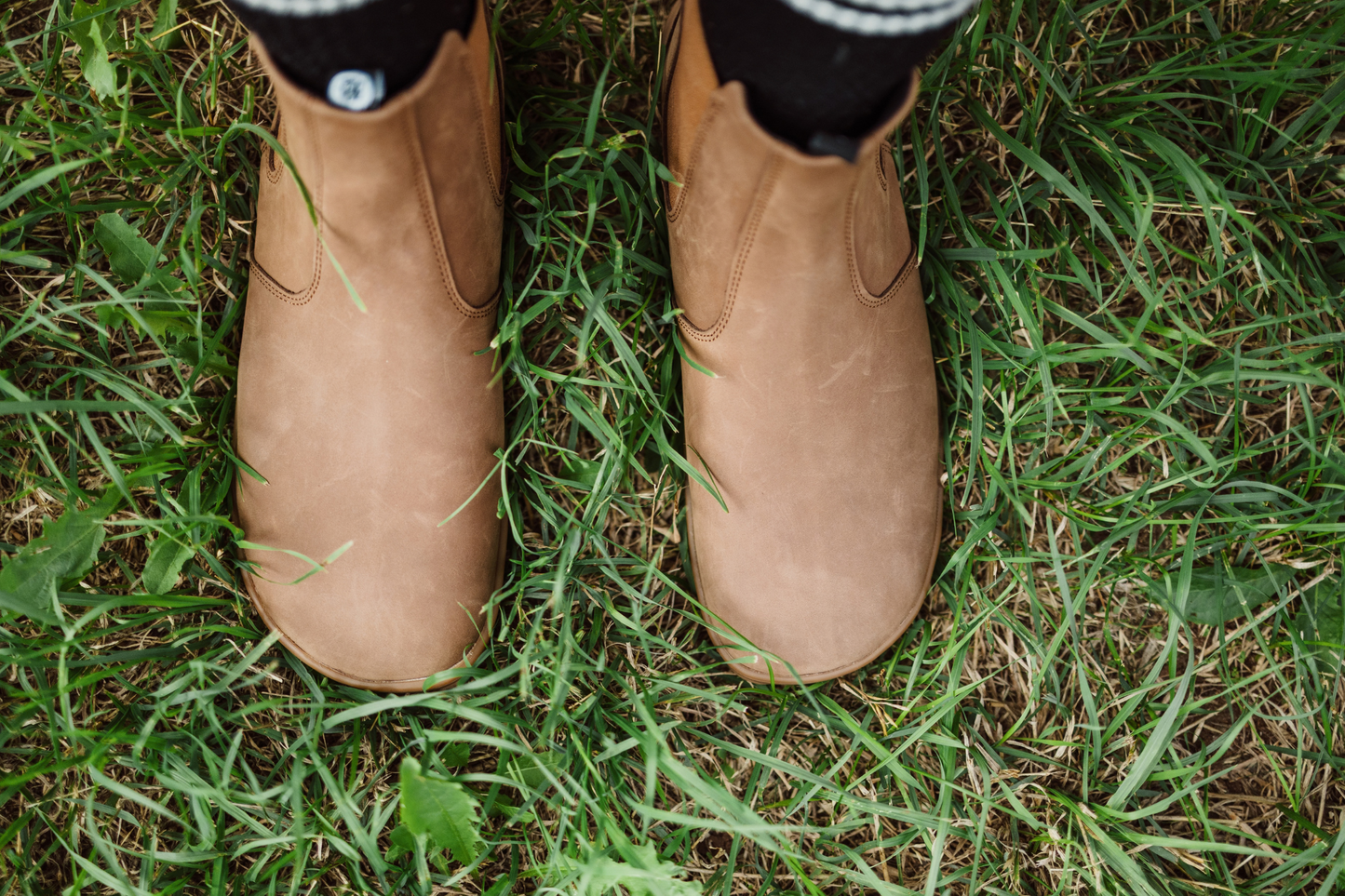 Brown PaperKrane foot-shaped chelsea boots viewed from above on grass with black and white socks. 