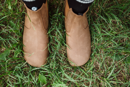 Brown PaperKrane foot-shaped chelsea boots viewed from above on grass with black and white socks. 
