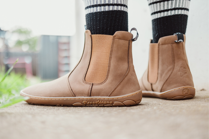 Brown leather PaperKrane barefoot Chelsea boots worn with black and white striped socks on a blurred outdoor background