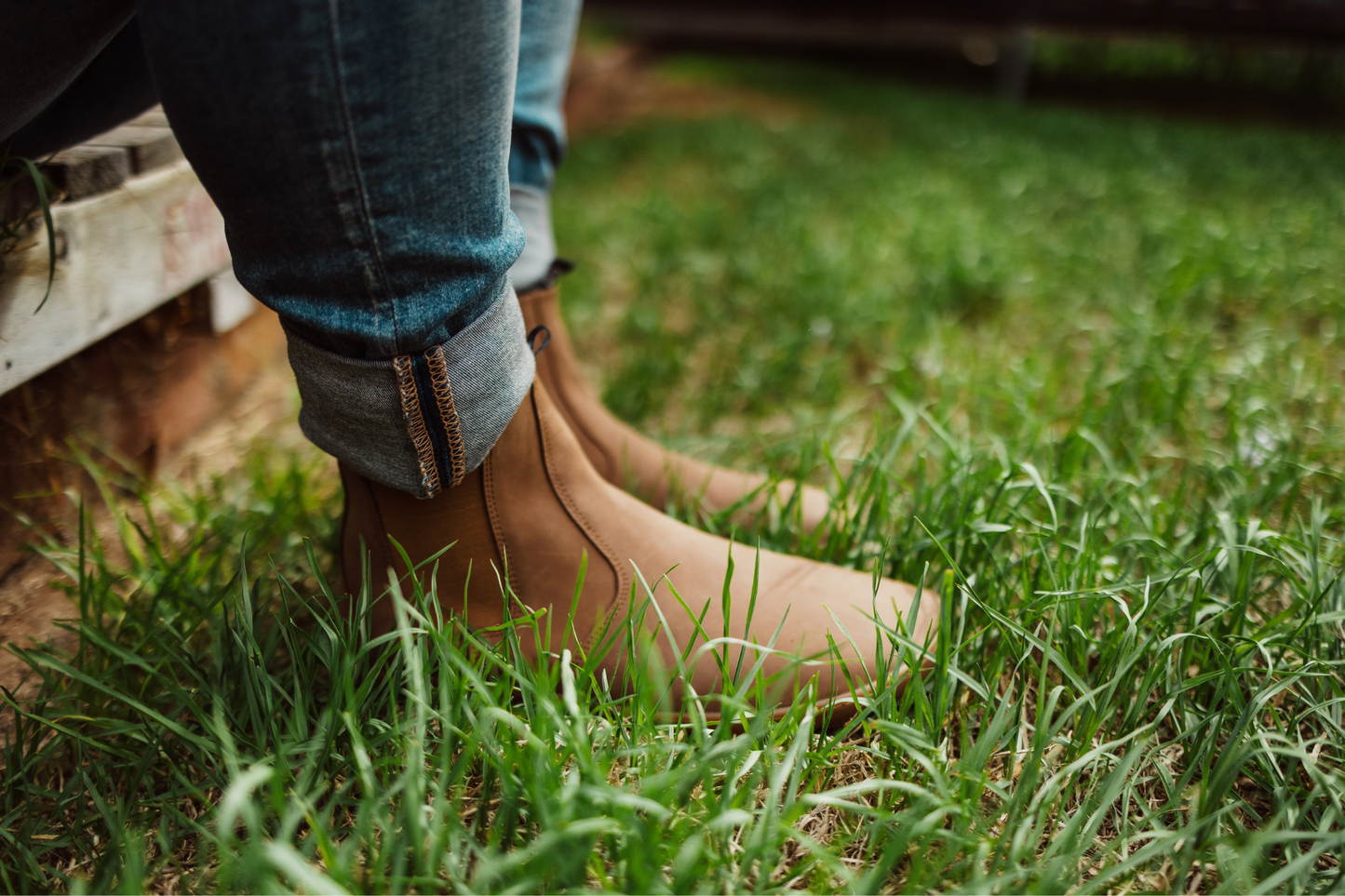 Person wearing brown leather barefoot PaperKrane chelsea boots and blue jeans on grass