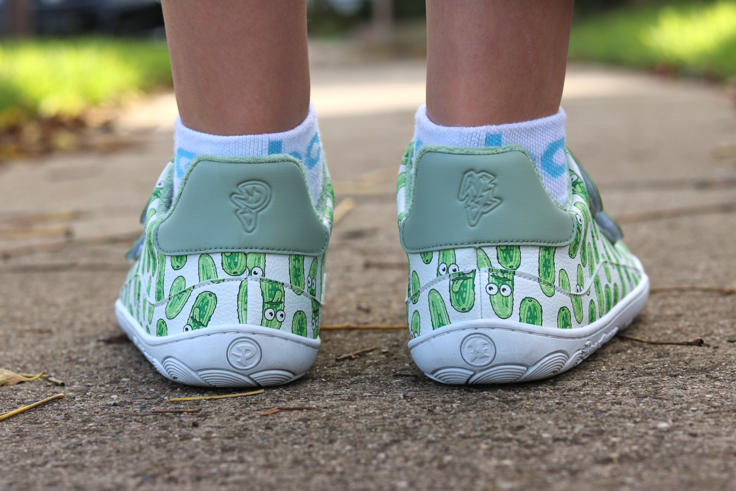 White velcro shoes with green pickle pattern on a concrete surface