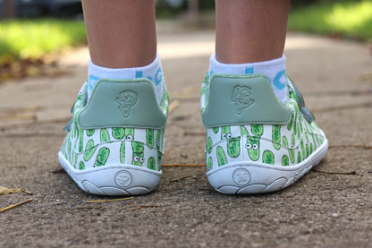 White velcro shoes with green pickle pattern on a concrete surface