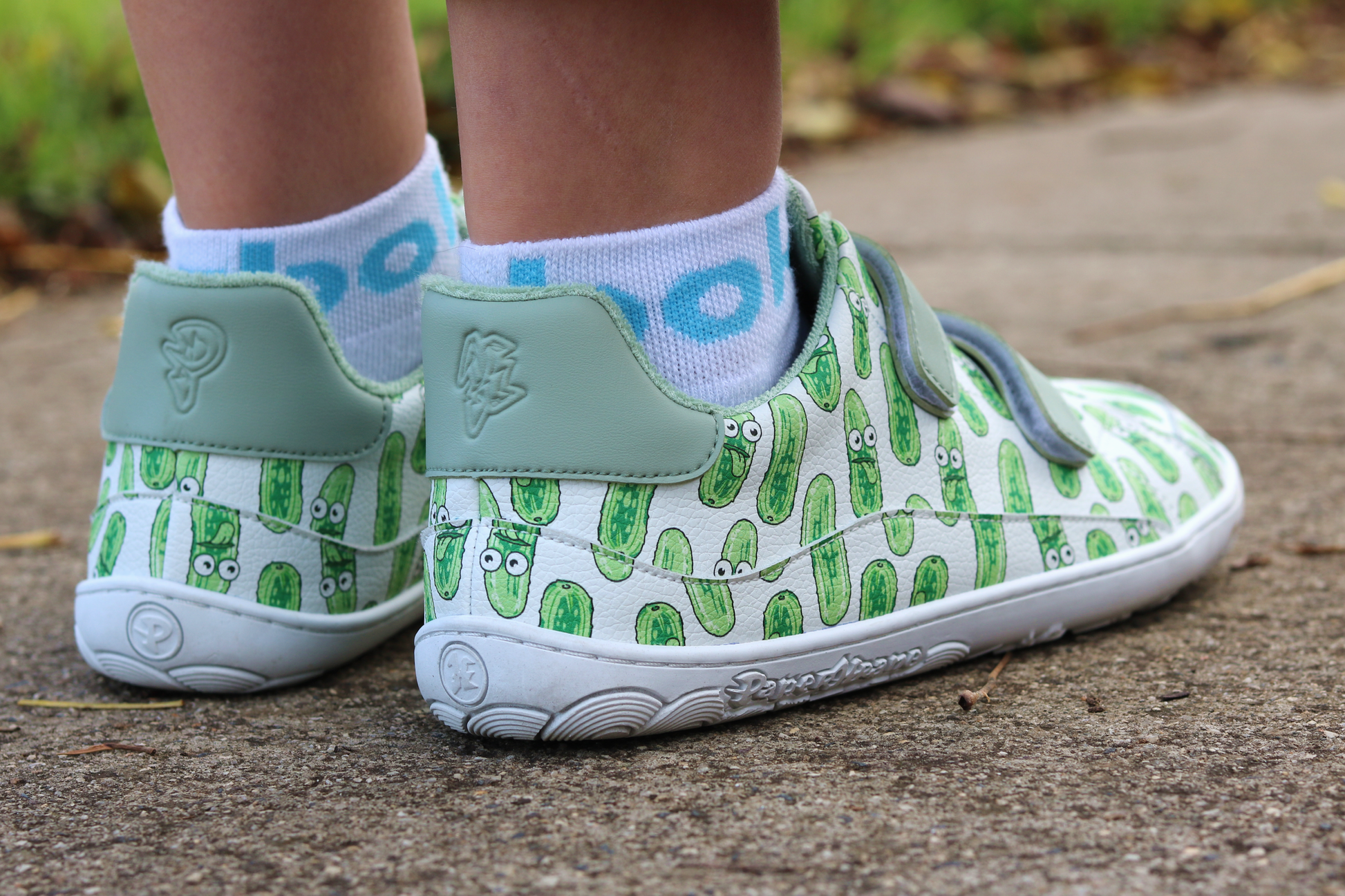 Children's shoes with green and white pickle pattern on a concrete surface