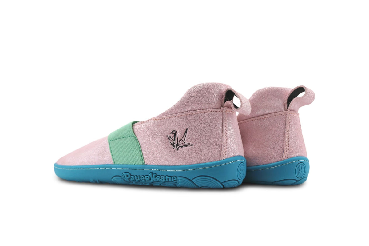 A pair of PaperKrane barefoot mary jane slip-ons in shimmery pink suede-leather with a mint green elastic strap and a bright teal-blue sole, shown from a side profile on a white background. There is a black Krane logo embossed on the side of the mary jane.