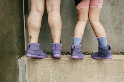 Two pairs of legs wearing purple high tops and pink shorts against a concrete wall.