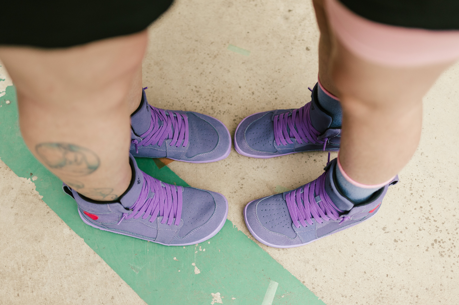 Purple sneakers worn on two people's feet with a light background