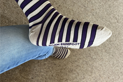 Pair of Roam Barefoot New Zealand made merino socks with purple and beige/grey stripes on a person's feet, with blue jeans, on carpet